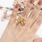 Anillo lazo dorado en mano femenina, detalle coqueto y elegante.