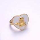 Anillo dorado con corazón blanco esmaltado y querubín dorado en relieve.