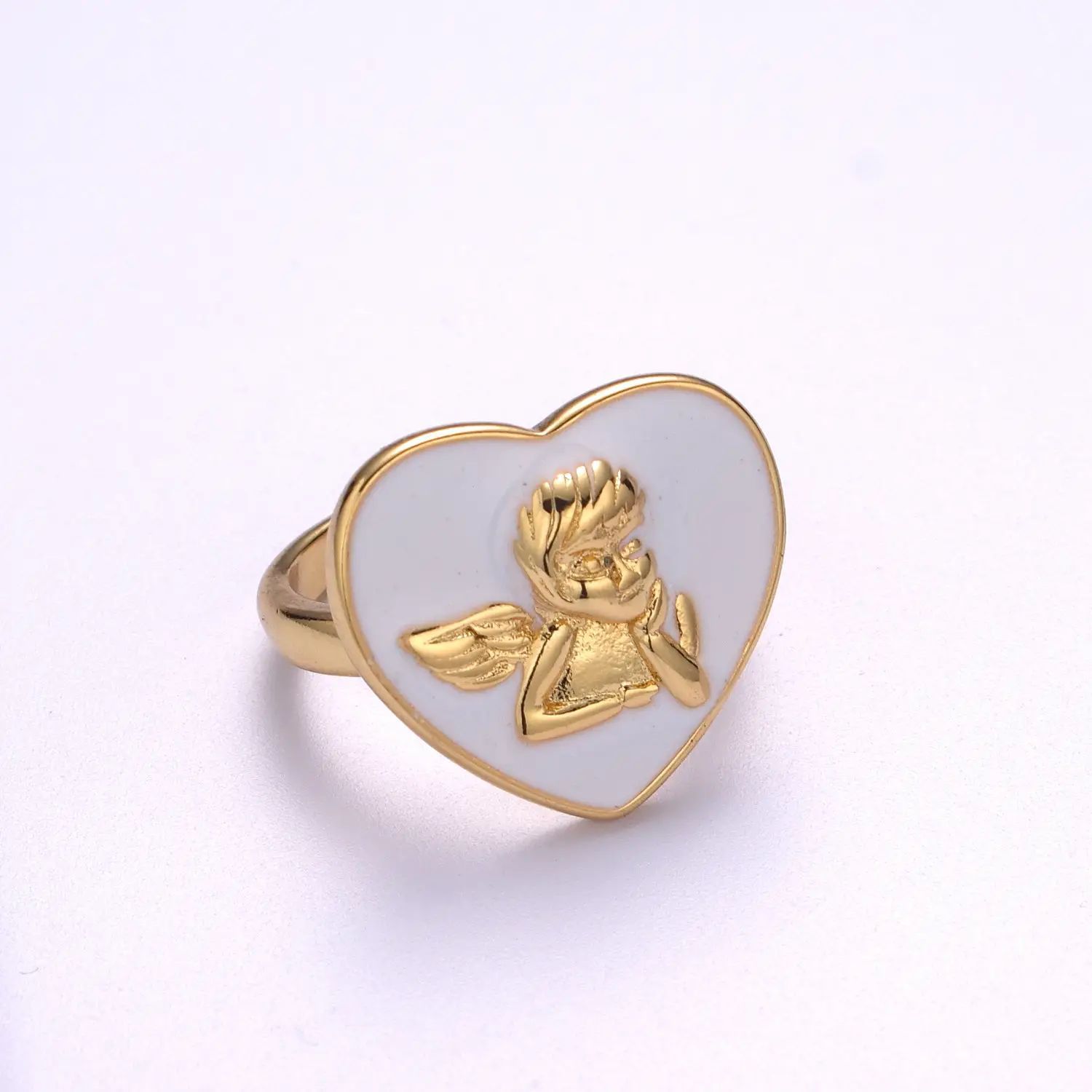Anillo dorado con corazón blanco esmaltado y querubín dorado en relieve.