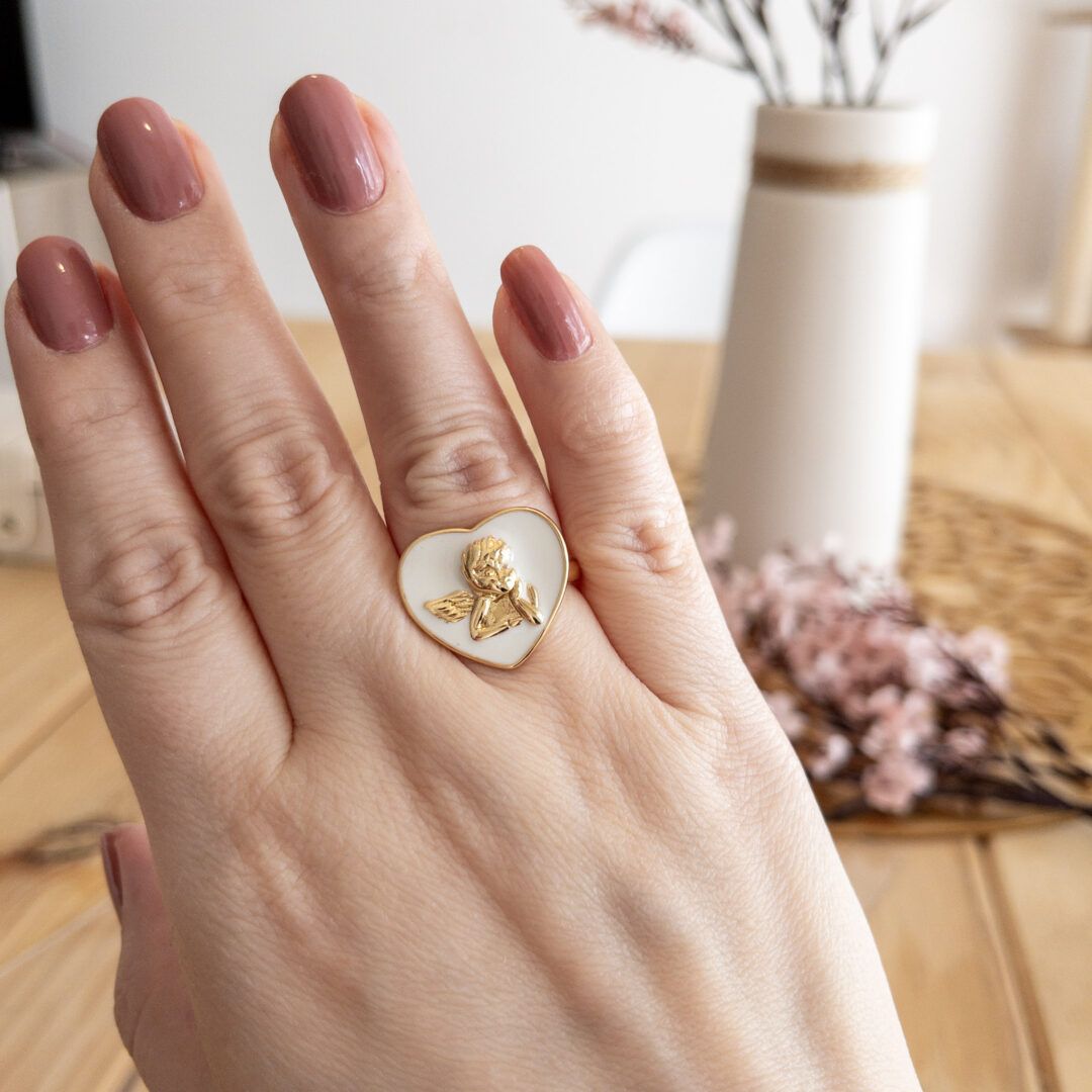 Anillo corazón con querubín blanco, puesto en dedo anular.