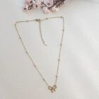 Collar dorado con lazo sobre fondo blanco texturizado y flores.